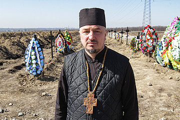 in Priester der Orthodoxen Kirche der Ukraine auf einem Friedhof mit frischen Gräbern gefallener Soldaten