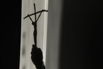 Dunkles Schattenbild von Hand, das ein Kreuz hochhält.