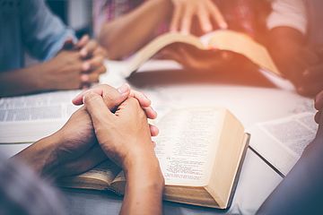 Hände auf Bibeln beim Beten