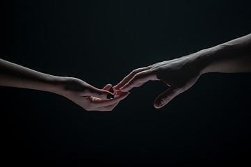 Zwei Hände greifen vor dunklem Hintergrund nacheinander