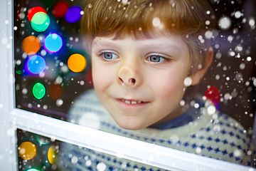 Kind drückt sich in weihnachtlicher Kulisse beim aus dem Fenster schauen die Nase platt.