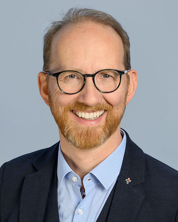 Porträt von Pfarrer Hofstetter, lächelnd im Anzug, mit Brille und Bart