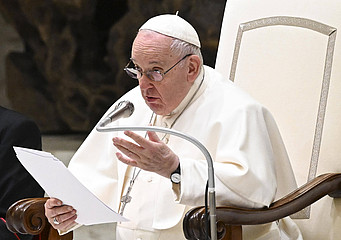 Papst Franziskus spricht sitzend in ein Mikrofon