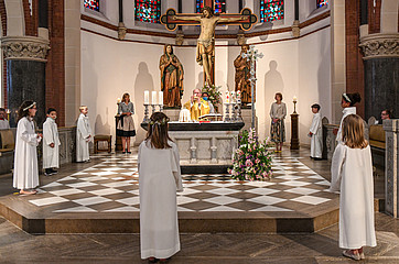Priester, Katecheten und Erstkommunionkinder in weißen Alben stehen mit Abstand im Kreis im Altarraum während der Eucharistiefeier bei der Messe zur Feier der Erstkommunion.