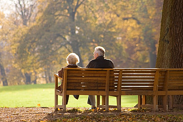 Zwei Senioren auf einer Parkbank mit dem Rücken zur Kamera