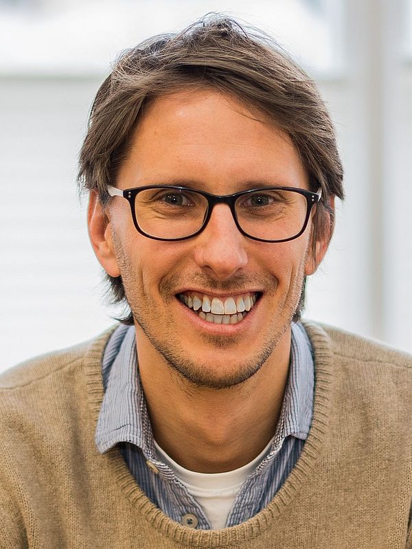 Porträt von Florian Wiedemann, lachend, braune Haare in hellbraunem Pulli mit Brille
