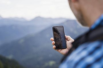 Ein Mensch wandert in den Bergen und schaut auf seinen Handy-Kompass