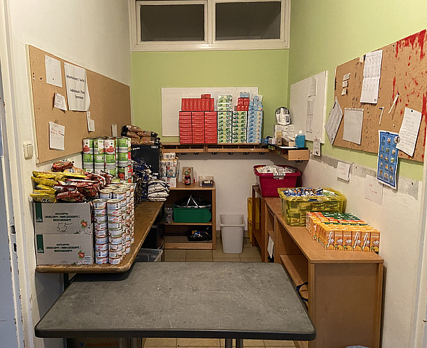 Hier sieht man die Lebensmittelausgabe in Haidhausen vor der Ausgabe an die Geflüchteten. Zu sehen ist ein kleiner Raum voller abgepackter Lebensmittel.