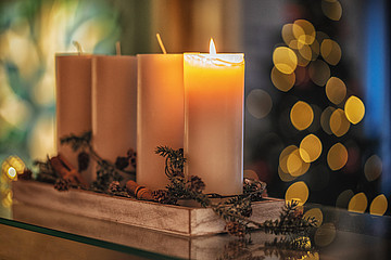 Vier weiße Kerzen stehen hintereinander, ein Docht brennt. 