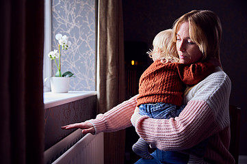 Frau mit Kind am Arm hält Hand über Heizung