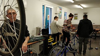 Flüchtlinge und ehrenamtliche Helfer machen gemeinsam Fahrräder wieder fahrtüchtig.