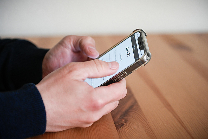 Ein Mann hält ein Smartphone in seinen Händen und betrachtet darauf den Chatbot "ChatGPT"