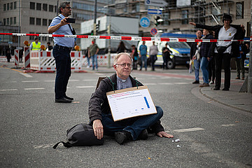 Jesuitenpater Jörg Alt sitzt mit Protest-Schild auf der Straße.