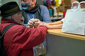 Zwei Menschen stehen am Tresen auf dem eine Tüte steht, ihre Hände berühren sich