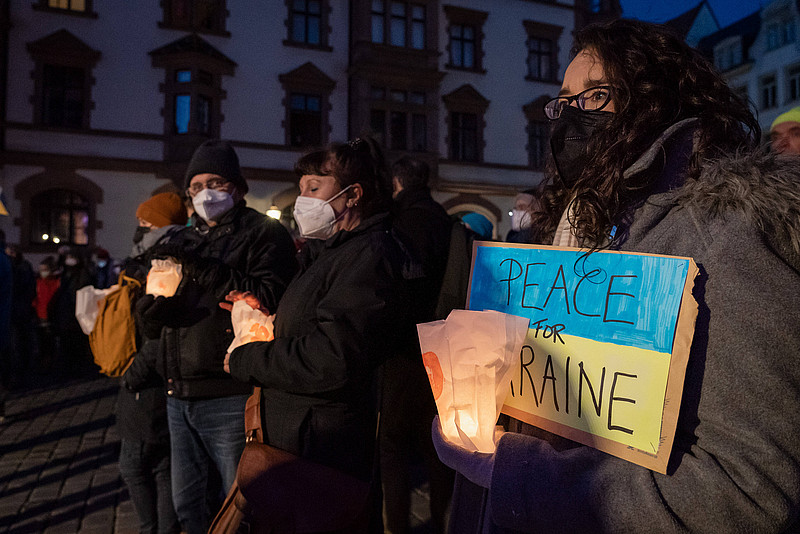 Eine Frau hält eine Kerze und ein blau-gelbes Schild mit der Aufschrift "Peace for Ukraine" in der Hand.