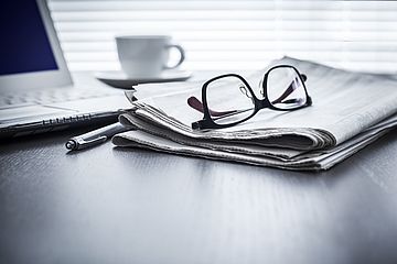 Brille liegt auf Zeitung, Laptop und Kaffetasse im Hintergrund