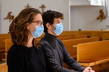 Junge Frau und junger Mann sitzen mit Maske in einer Kirche