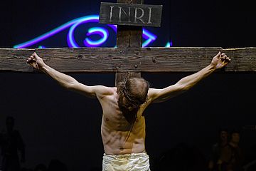 Ein Mann spielt Jesus, man sieht seinen Oberkörper wie er am Kreuz hängt, den Kopf gesenkt
